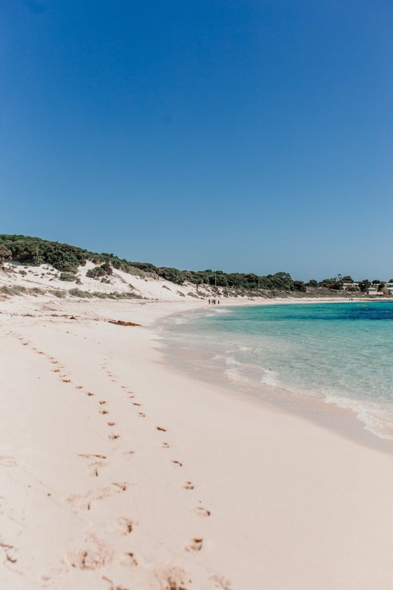 Tranquil beach scene with footprints leading to the ocean under a vibrant blue sky.